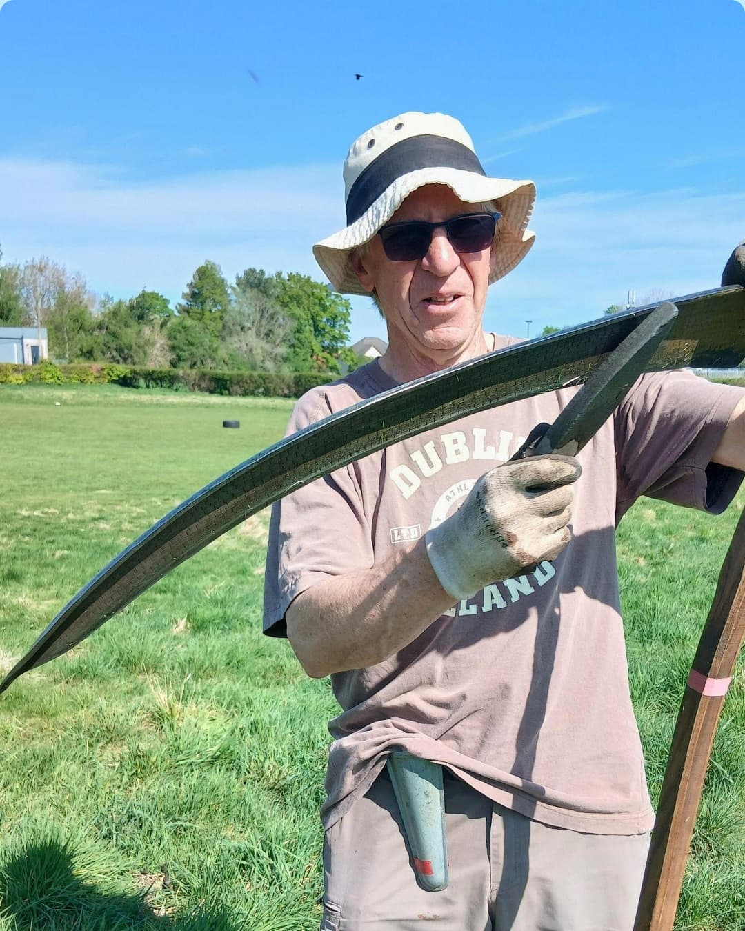 Volunteer demonstrating an Austrian scythe in a grassy community space